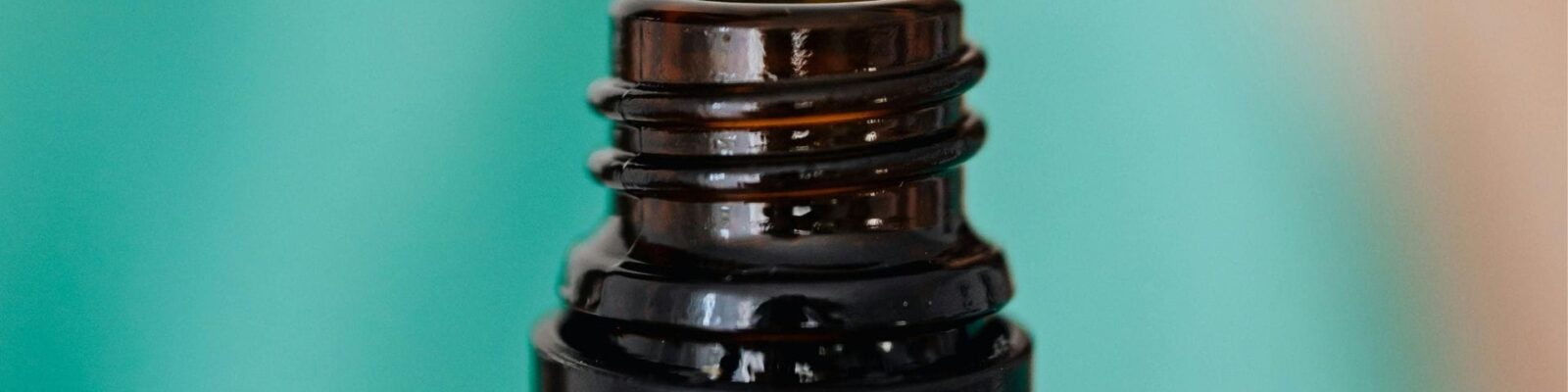 Close-up of an amber glass bottle's threaded neck against a teal background.