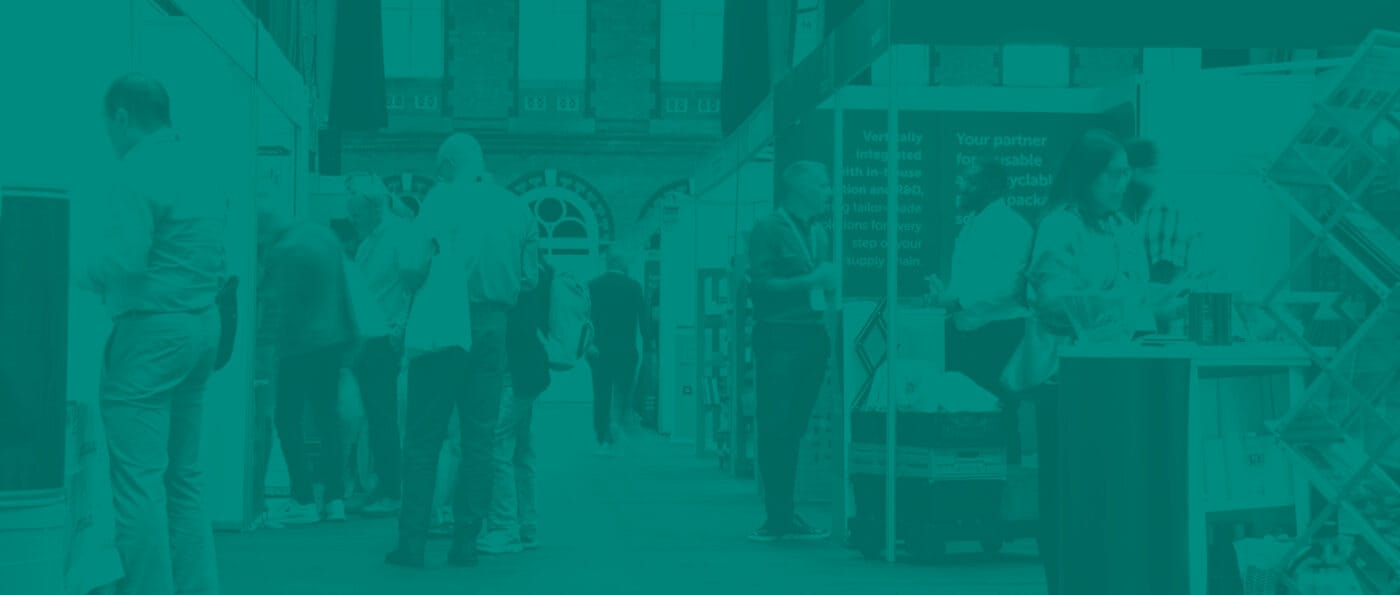 A busy exhibition floor shows people gathering in aisles, in between shell scheme stand. The image is overlayed with a teal-coloured tint.